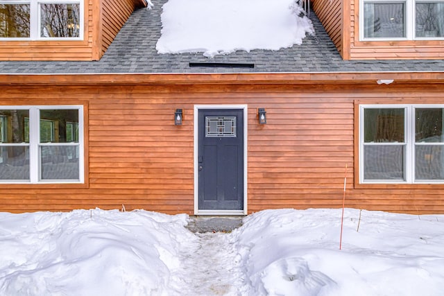 snow covered property entrance with a shingled roof