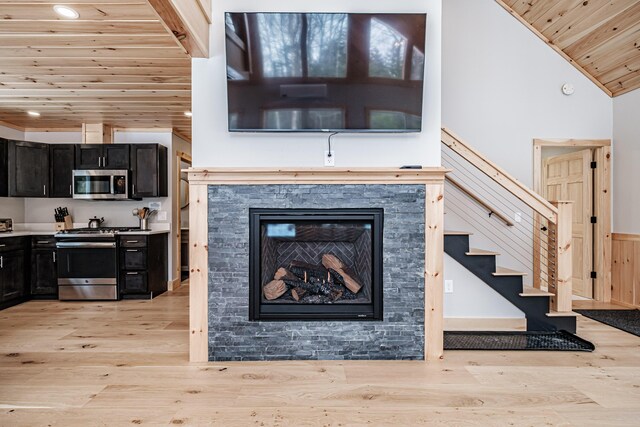 living area with lofted ceiling, a stone fireplace, wood ceiling, and light wood-style floors