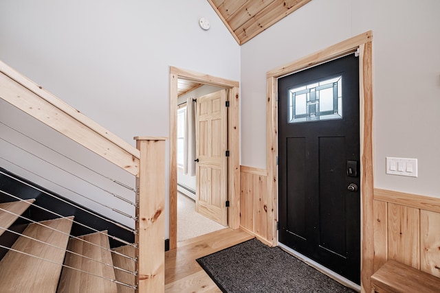 foyer entrance with lofted ceiling, a wainscoted wall, wood walls, wood finished floors, and baseboard heating