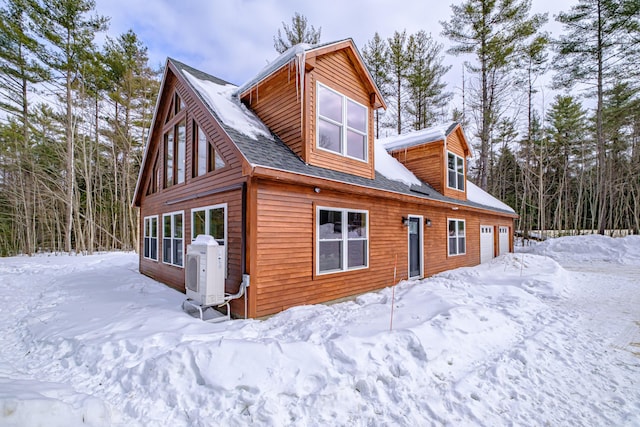 snow covered rear of property with a garage and ac unit