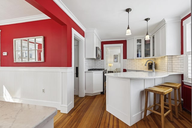 kitchen with a wainscoted wall, wood finished floors, white cabinets, appliances with stainless steel finishes, and glass insert cabinets