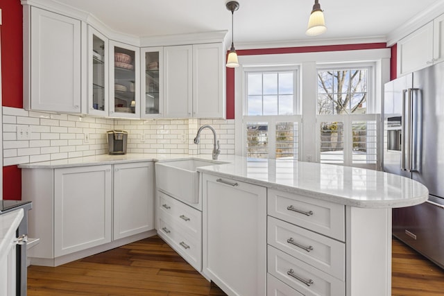 kitchen featuring a peninsula, a sink, white cabinetry, high end fridge, and glass insert cabinets