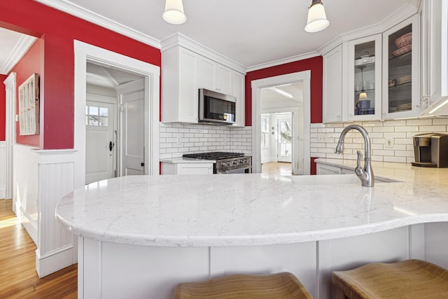 kitchen with white cabinets, ornamental molding, stainless steel appliances, and light stone counters