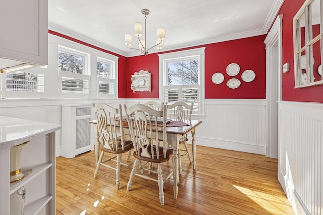 dining space with ornamental molding, wainscoting, light wood finished floors, and an inviting chandelier