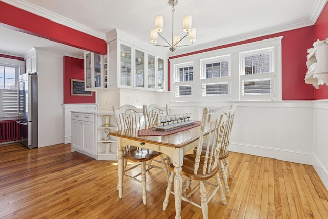 dining room featuring a chandelier, wainscoting, light wood-type flooring, and crown molding