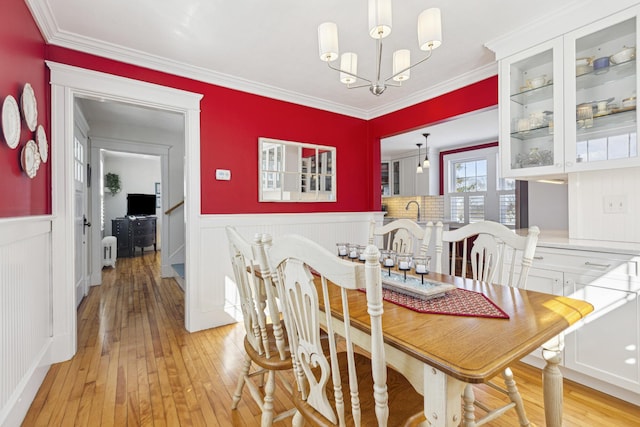 dining area featuring a chandelier, a wainscoted wall, light wood-style floors, and ornamental molding