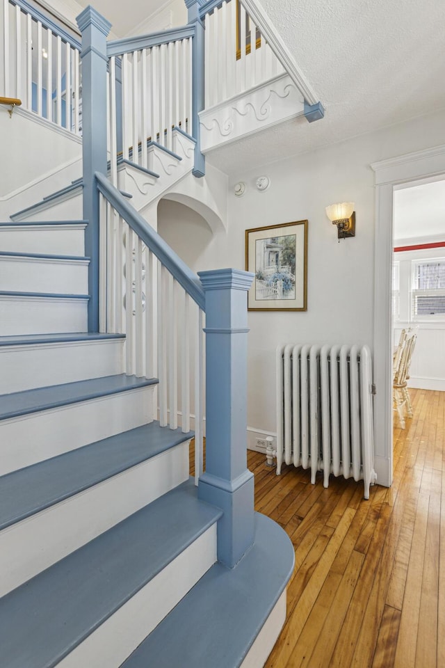 stairway featuring baseboards, hardwood / wood-style floors, and radiator heating unit