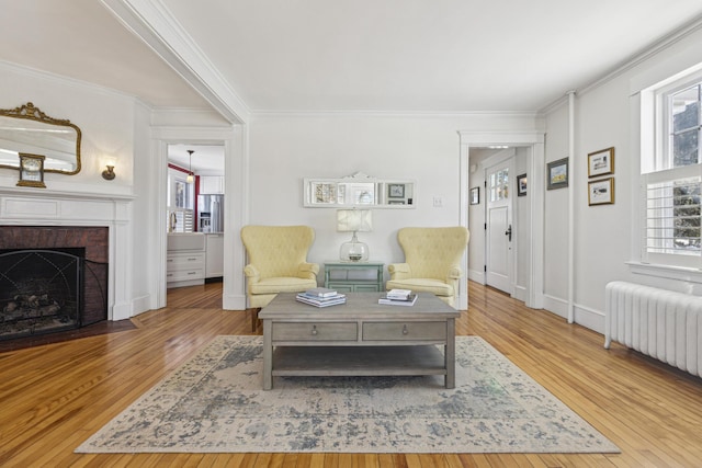 living area with a brick fireplace, radiator heating unit, wood-type flooring, and crown molding