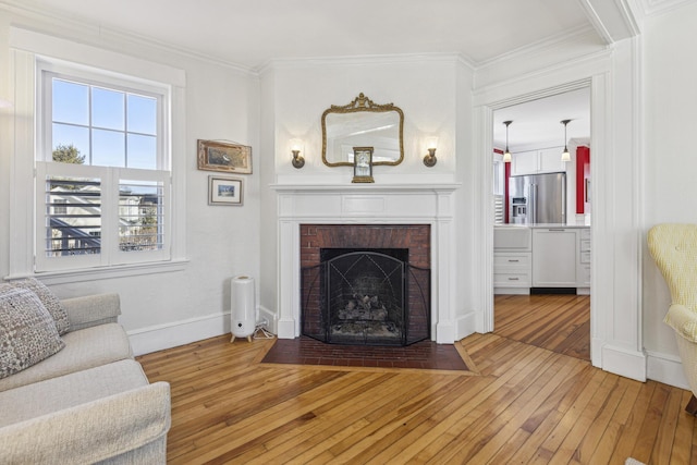 living room featuring ornamental molding, a brick fireplace, baseboards, and hardwood / wood-style floors