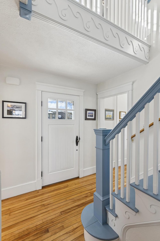 foyer with light wood-type flooring, baseboards, stairway, and a textured ceiling