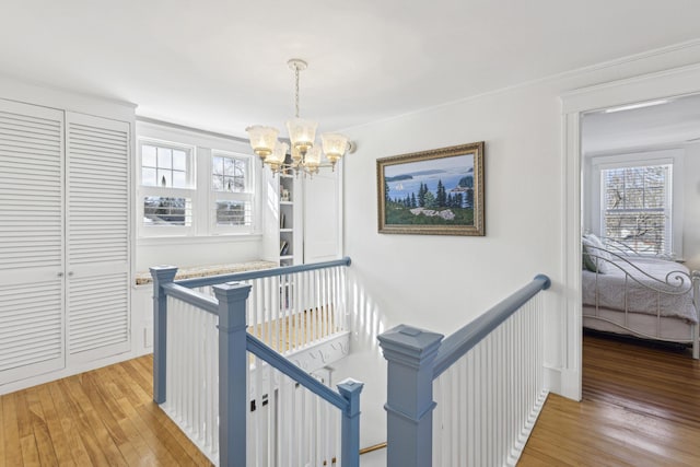 hallway featuring a wealth of natural light, light wood-style flooring, a chandelier, and an upstairs landing