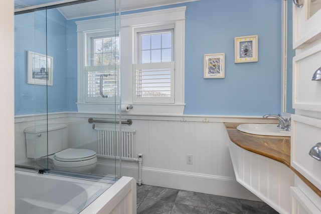 full bath featuring wainscoting, toilet, radiator, a shower with shower door, and vanity