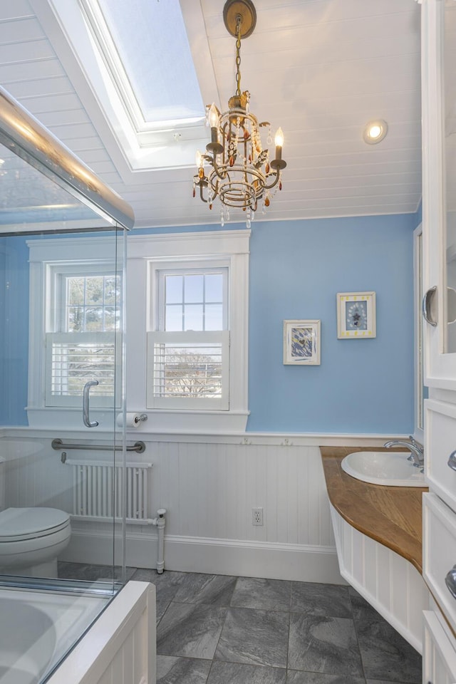 full bath with a notable chandelier, toilet, a shower with shower door, wainscoting, and vanity