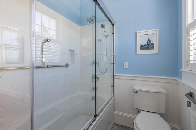 full bath with a wainscoted wall, toilet, a wealth of natural light, and enclosed tub / shower combo