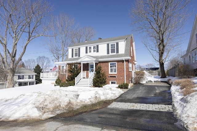 colonial inspired home featuring driveway, a shingled roof, and brick siding