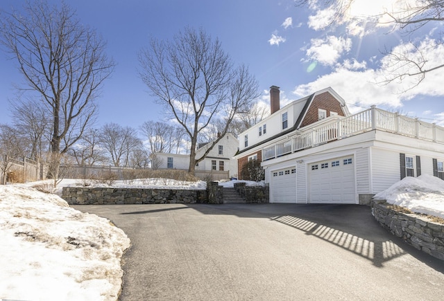 view of snowy exterior with driveway, an attached garage, a chimney, and a gambrel roof