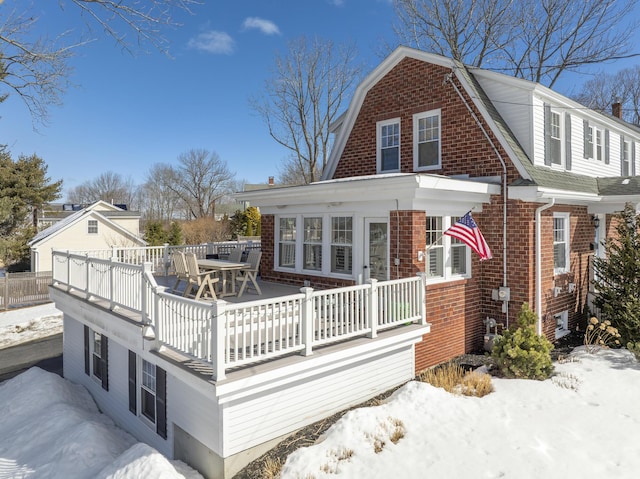 exterior space with a deck, brick siding, outdoor dining area, and a gambrel roof