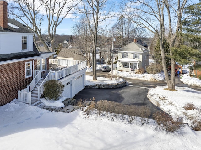 yard covered in snow featuring a garage, a residential view, stairway, and a deck