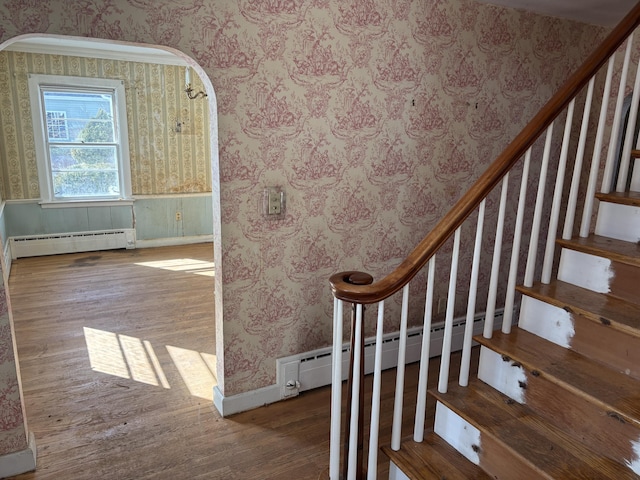 stairs featuring arched walkways, a baseboard radiator, and wallpapered walls