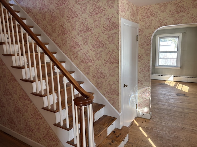 stairway featuring wallpapered walls, baseboard heating, and wood finished floors