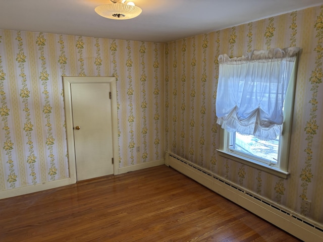 empty room with a baseboard heating unit, baseboards, wood finished floors, and wallpapered walls