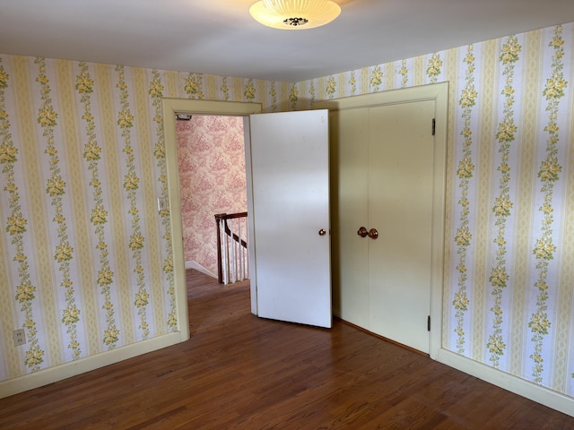 unfurnished bedroom featuring a closet, wood finished floors, baseboards, and wallpapered walls