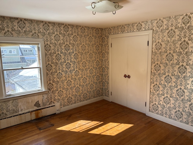 spare room featuring a baseboard heating unit, wood finished floors, baseboards, and wallpapered walls