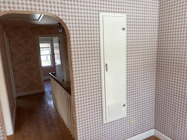 hallway with arched walkways, wood finished floors, baseboards, and wallpapered walls