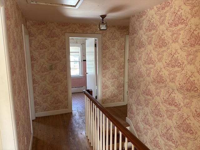 hallway featuring baseboard heating, an upstairs landing, wood finished floors, baseboards, and wallpapered walls