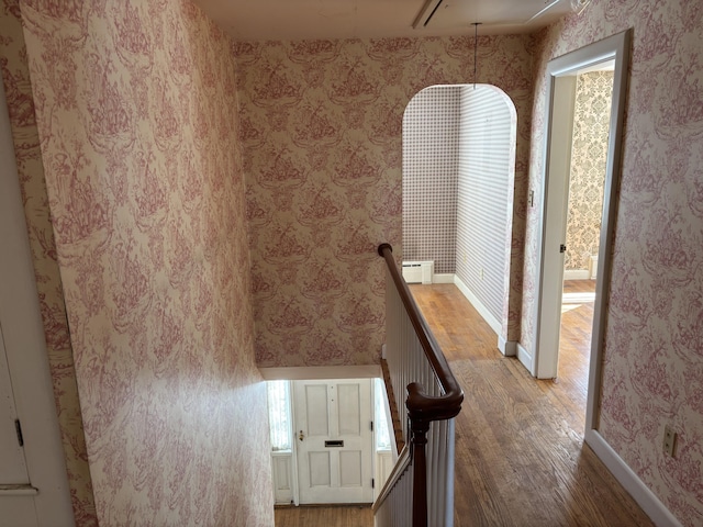 hallway featuring a baseboard radiator, wood finished floors, an upstairs landing, baseboards, and wallpapered walls