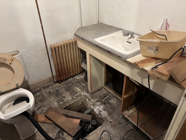 bathroom featuring a textured wall, toilet, a sink, and radiator heating unit