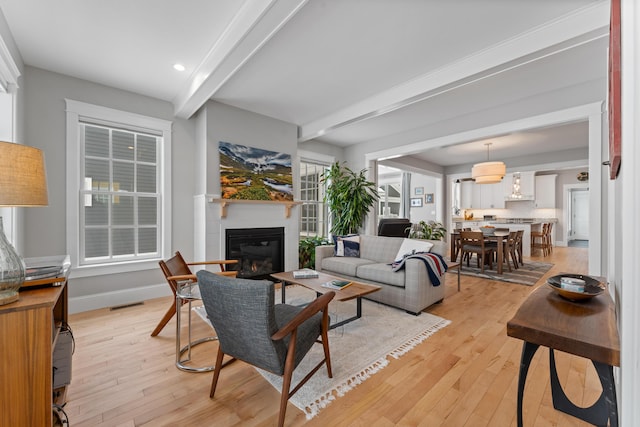 living area featuring light wood-style floors, baseboards, visible vents, and beamed ceiling