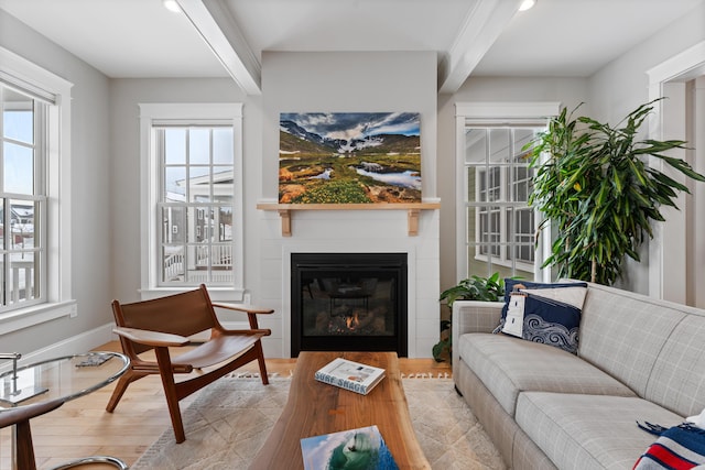 living room featuring light wood-style floors, baseboards, beam ceiling, and a glass covered fireplace