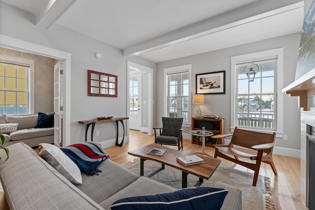 living area featuring baseboards, light wood finished floors, beamed ceiling, and a healthy amount of sunlight