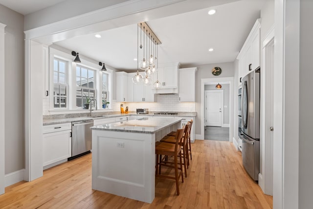 kitchen featuring a kitchen island, stainless steel appliances, white cabinetry, pendant lighting, and a sink