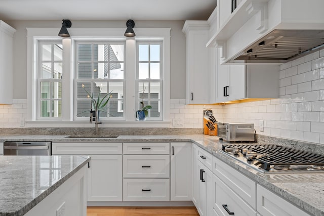 kitchen featuring wall chimney range hood, appliances with stainless steel finishes, white cabinets, and a sink