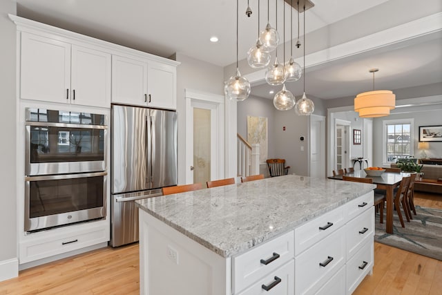 kitchen featuring stainless steel appliances, a center island, white cabinetry, and hanging light fixtures