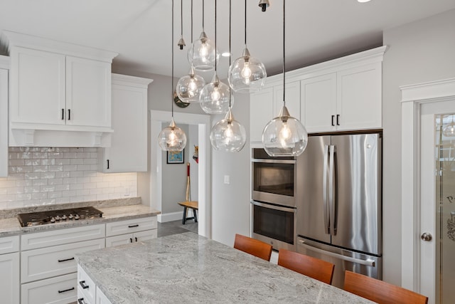 kitchen featuring a kitchen breakfast bar, light stone countertops, stainless steel appliances, white cabinetry, and pendant lighting