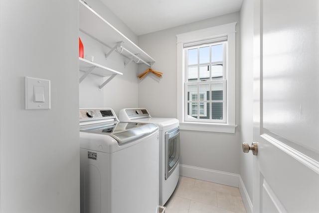 clothes washing area featuring light tile patterned floors, laundry area, washing machine and clothes dryer, and baseboards