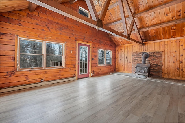 unfurnished living room featuring vaulted ceiling with beams, baseboard heating, a wood stove, wood walls, and wood finished floors