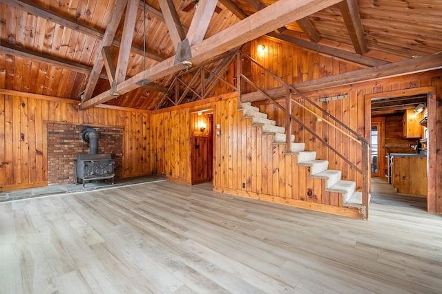 unfurnished living room with a wood stove, wood walls, wood finished floors, wooden ceiling, and stairs