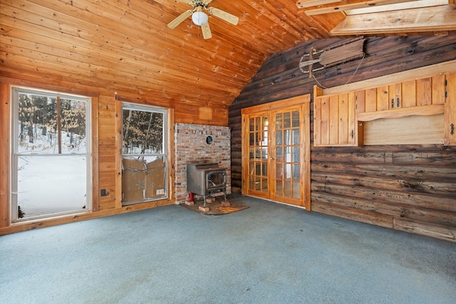 unfurnished living room featuring ceiling fan, wooden walls, vaulted ceiling, carpet, and a wood stove