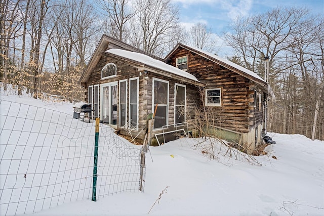 view of snowy exterior featuring a sunroom and log exterior