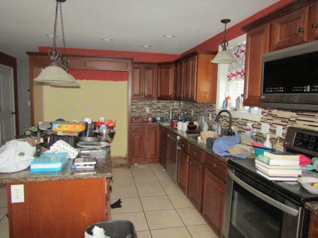 kitchen featuring a center island, decorative light fixtures, light tile patterned floors, stainless steel appliances, and tasteful backsplash