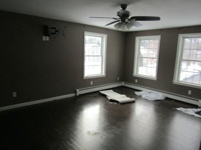 unfurnished room with a ceiling fan, baseboard heating, baseboards, and wood finished floors