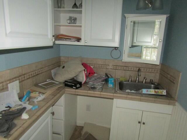 kitchen with tile countertops, tasteful backsplash, white cabinets, and a sink