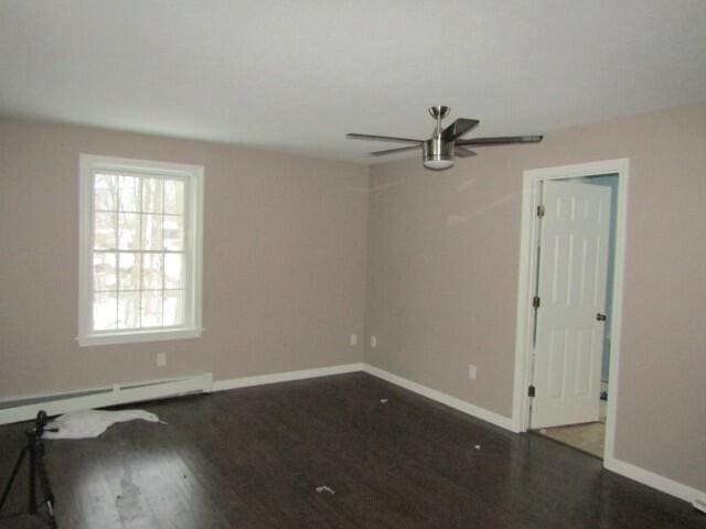 empty room featuring dark wood-type flooring, a baseboard radiator, ceiling fan, and baseboards