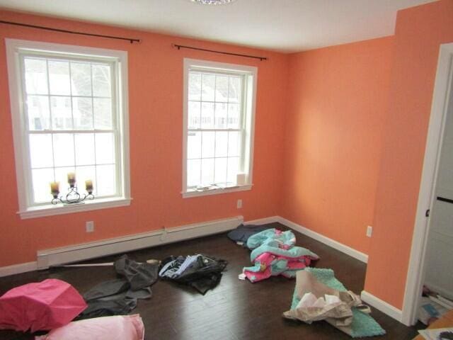 unfurnished room with baseboards, a baseboard heating unit, and wood finished floors