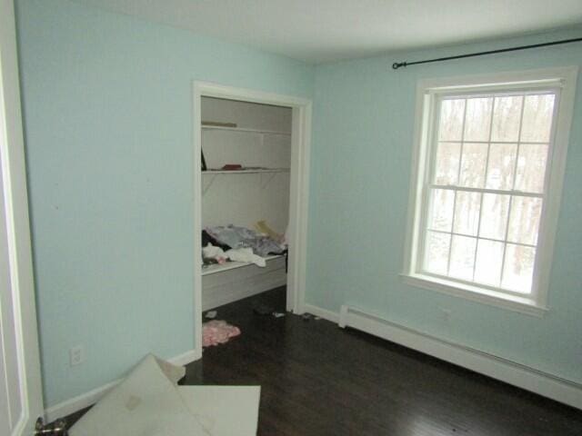 bedroom featuring a closet, a baseboard radiator, dark wood finished floors, and baseboards