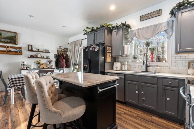 kitchen featuring gray cabinetry, a sink, light countertops, stainless steel dishwasher, and a center island